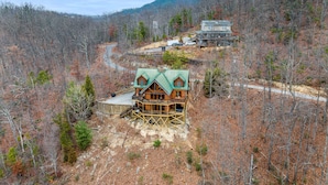 Eine Holzhütte mit grüner Dachdeckung, umgeben von bewaldetem Gelände und einem Berg im Hintergrund.