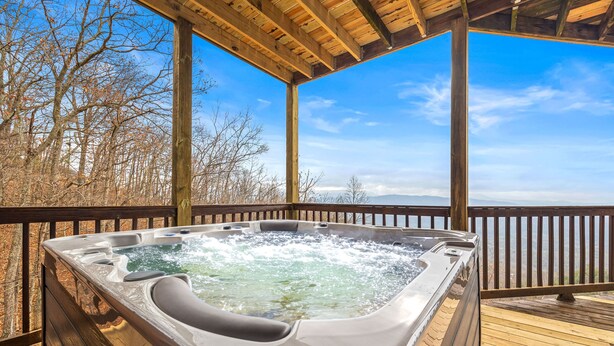 Ein Whirlpool auf einer Holzterrasse mit Holzwand und freiem Blick auf Bäume und Berge im Hintergrund.