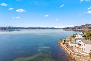 A lakeside property with a dock, a small boat, and a house with a green roof. - Belfair Beach House in Belfair (Belfair)