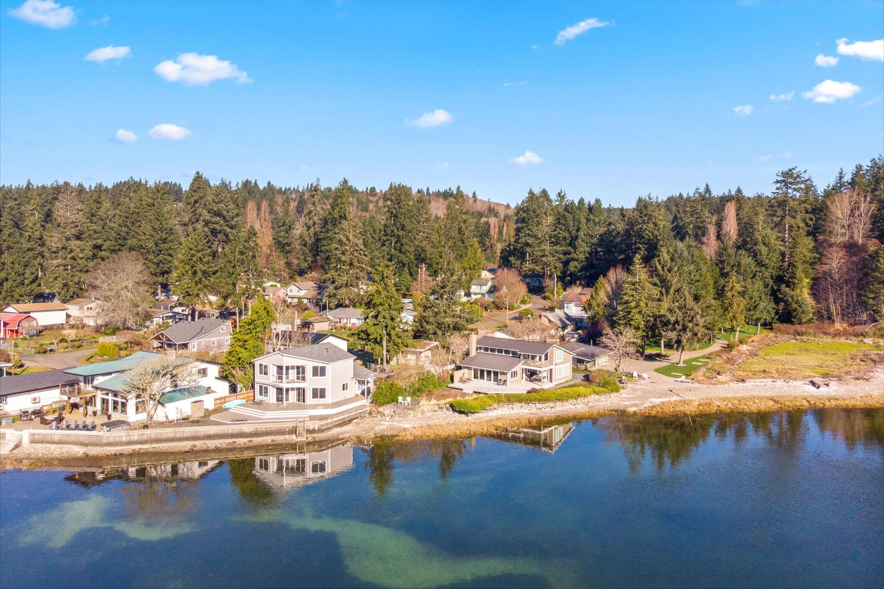 Un quartier résidentiel au bord d’un lac, avec des maisons, un quai et une colline boisée en arrière-plan.