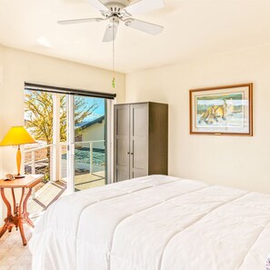 A bedroom with a bed, a ceiling fan, a wardrobe, a framed picture, and a view through a sliding glass door. - Belfair Beach House in Belfair (Belfair)