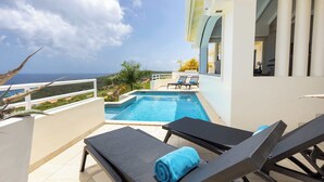 A poolside area with lounge chairs and a view of the sea. - Shoreline Harmony at Villa Solana (Rif St Marie)