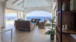 A spacious living area with a view of the sea, furnished with wicker furniture and a potted plant. - Shoreline Harmony at Villa Solana (Rif St Marie)