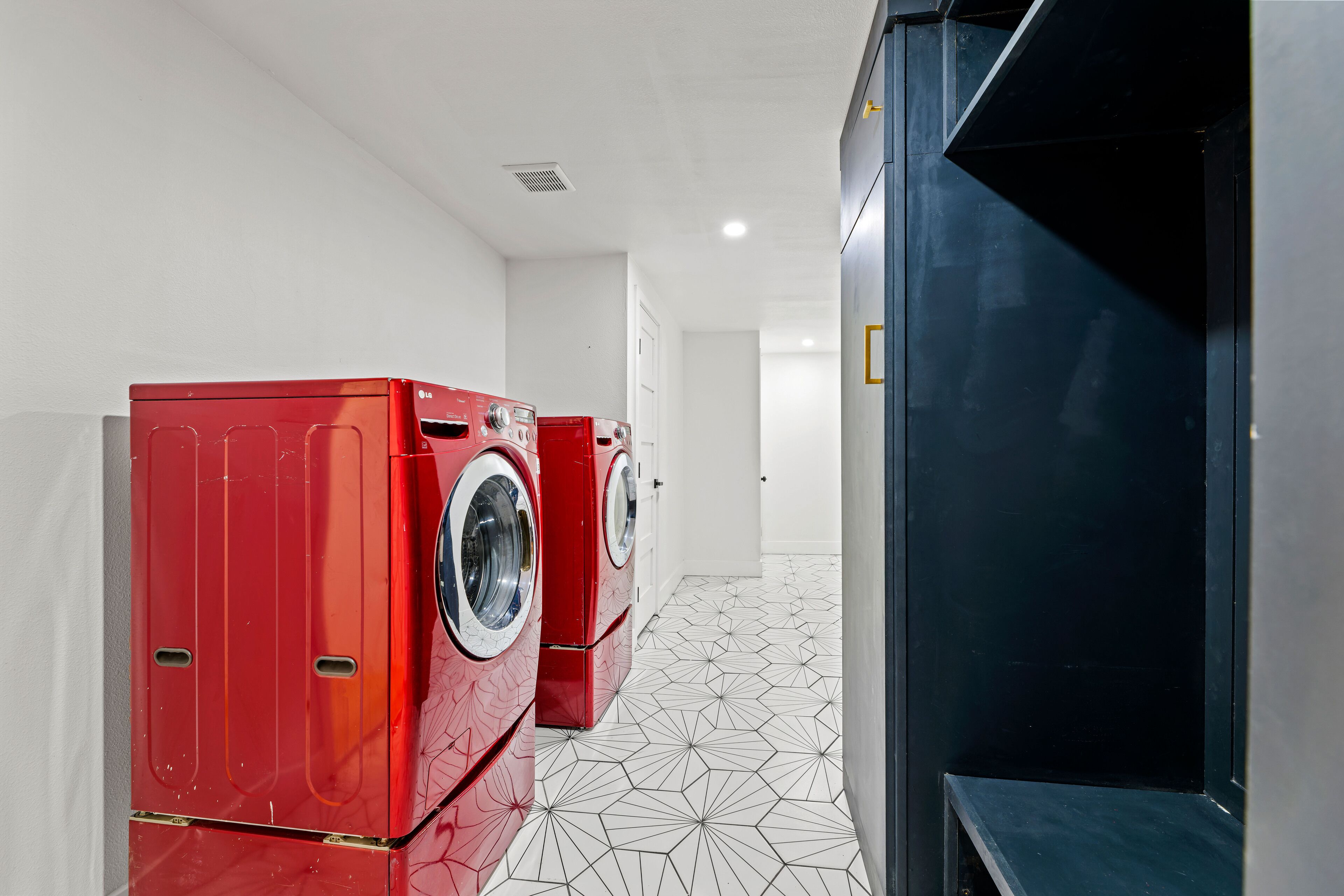 A laundry room with two red washing machines and a black cabinet.