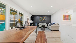 A modern living room with a wooden dining table, a sofa, and a coffee table. There is a TV mounted on the wall and a colorful abstract painting above the sofa. - Tipperary Oasis: 3 Beds & a Private Pool (Dallas)