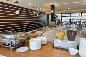A buffet setup with various food items, a large wall with horizontal lines, and a seating area with tables and chairs. - Single-story holiday homes very close to the beach (Lazy)
