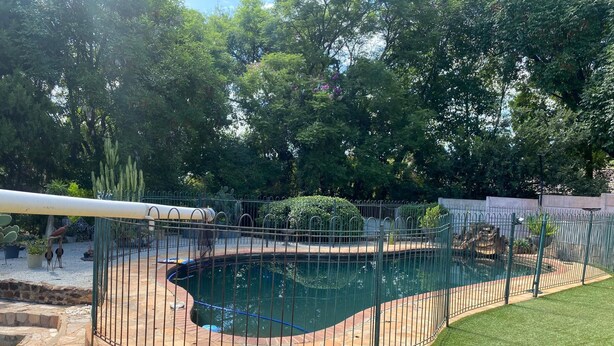 A swimming pool with a stone border and a metal fence. - Pristine 1 Bed Cottage in Northern Suburbs - 2222 (Harare)