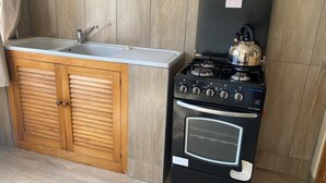 A compact kitchen with a wooden cabinet, a sink, and a black stove with a kettle. - Pristine 1 Bed Cottage in Northern Suburbs - 2222 (Harare)