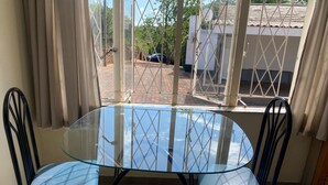 A glass-top table with two black chairs, a window with metal bars, and a view of a street and buildings outside. - Pristine 1 Bed Cottage in Northern Suburbs - 2222 (Harare)