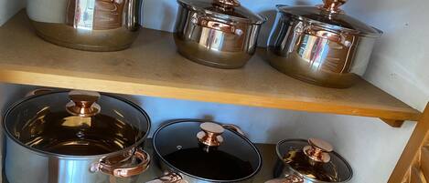 A kitchen shelf with stainless steel cookware, including pots and pans with copper handles.