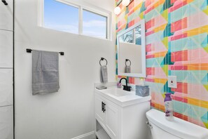 Une salle de bain avec un lavabo blanc, un miroir et un mur orné d’un motif géométrique coloré.