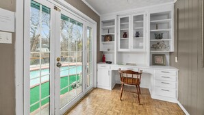 A room with a wooden herringbone floor, a white desk with drawers, a chair, and a built-in white shelving unit with decorative items. - White Rock Poolside Retreat- 4 Beds & a Private Pool (Dallas)