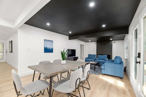A modern living room with a dining area, a blue sofa, and a flat-screen TV.