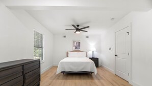 A bedroom with a bed, a dresser, a ceiling fan, a nightstand, and a door. - Forest Hill Family Hideaway- 4-Bed Retreat (Dallas)