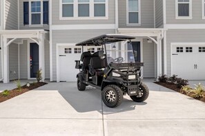A golf cart parked in a driveway in front of a two-story building with garage doors.