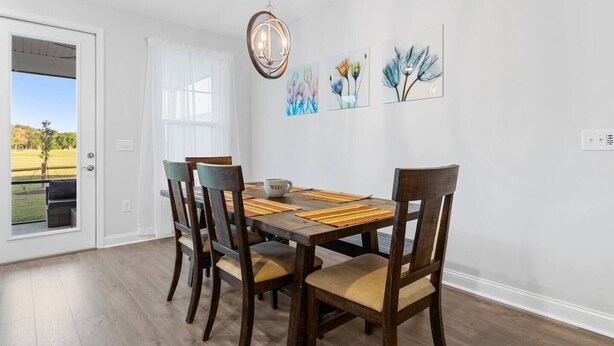 A dining area with a wooden table, four chairs, a chandelier, and three wall-mounted paintings. - Tee & Sea Paradise- Pool- Slps 11- Golf View-Grill (North Myrtle Beach)