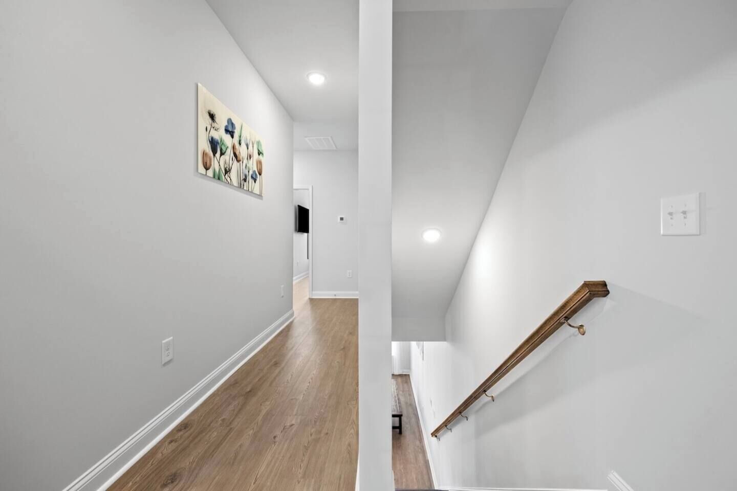 A modern interior with a wooden floor, white walls, and a staircase with a wooden handrail.