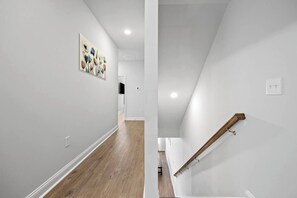 Un interior moderno con piso de madera, paredes blancas y una escalera con barandilla de madera.