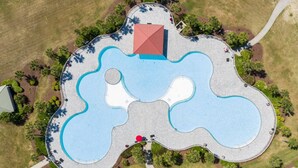 An aerial view of a property with a large irregularly shaped pool, surrounded by a paved walkway and greenery. - Tee & Sea Paradise- Pool- Slps 11- Golf View-Grill (North Myrtle Beach)