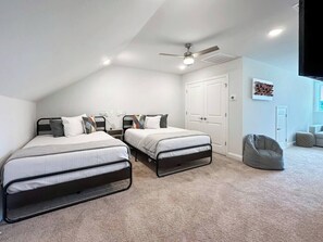 A bedroom with two beds, a ceiling fan, a white door, and a bean bag chair.