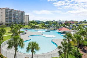A hotel with a large swimming pool, palm trees, and a view of the surrounding area.