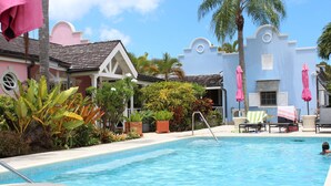 A swimming pool with lounge chairs and umbrellas, surrounded by tropical plants and a building with a pink and blue facade. - Beachcombers villa, Porters Court, Fairmont beach passes, few meters to Lonestar (Porters)