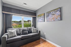 Una habitación con un sofá gris, una ventana con cortinas y dos cuadros en la pared.