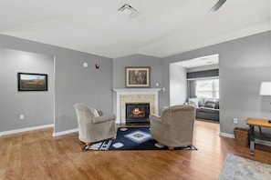 Een woonkamer met een open haard, twee fauteuils, een vloerkleed en een bank.