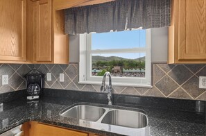 Una cocina con un lavamanos doble, armarios de madera, una cafetera y un ventanal con vistas a un paisaje verde.