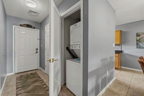 A hallway with a white door, a laundry room with a washing machine, and a kitchen area with a countertop and cabinets.