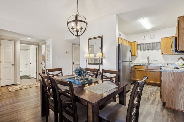 A dining area with a wooden table and chairs, a chandelier, and a kitchen in the background. - Two bedroom, two bathroom condo overlooking the Old Mill District (Pigeon Forge)