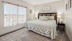 A bedroom with a large bed, two bedside tables, a window with sheer curtains, and a decorative wall piece. - 3 BR | City View | Updated | Free Dollywood Ticket | Indoor Pool (Pigeon Forge)
