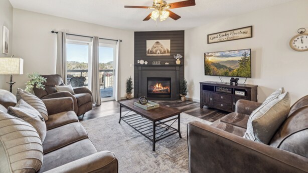A living room with a fireplace, leather sofas, a coffee table, and a ceiling fan. - 3 BR | City View | Updated | Free Dollywood Ticket | Indoor Pool (Pigeon Forge)