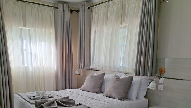 A modern bedroom with a bed, curtains, a bedside table, and a ceiling fan.