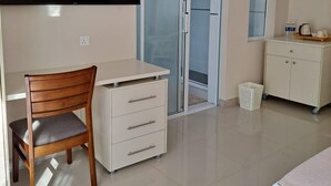 A modern room with a desk, chair, wardrobe, and a sliding glass door leading to a balcony.