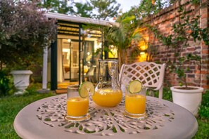 A table with three glasses of orange juice and a pitcher, set outdoors with a brick wall and greenery in the background. - Kamuzi Exquisite Tiny Home Near Airport - 2217 (Harare)