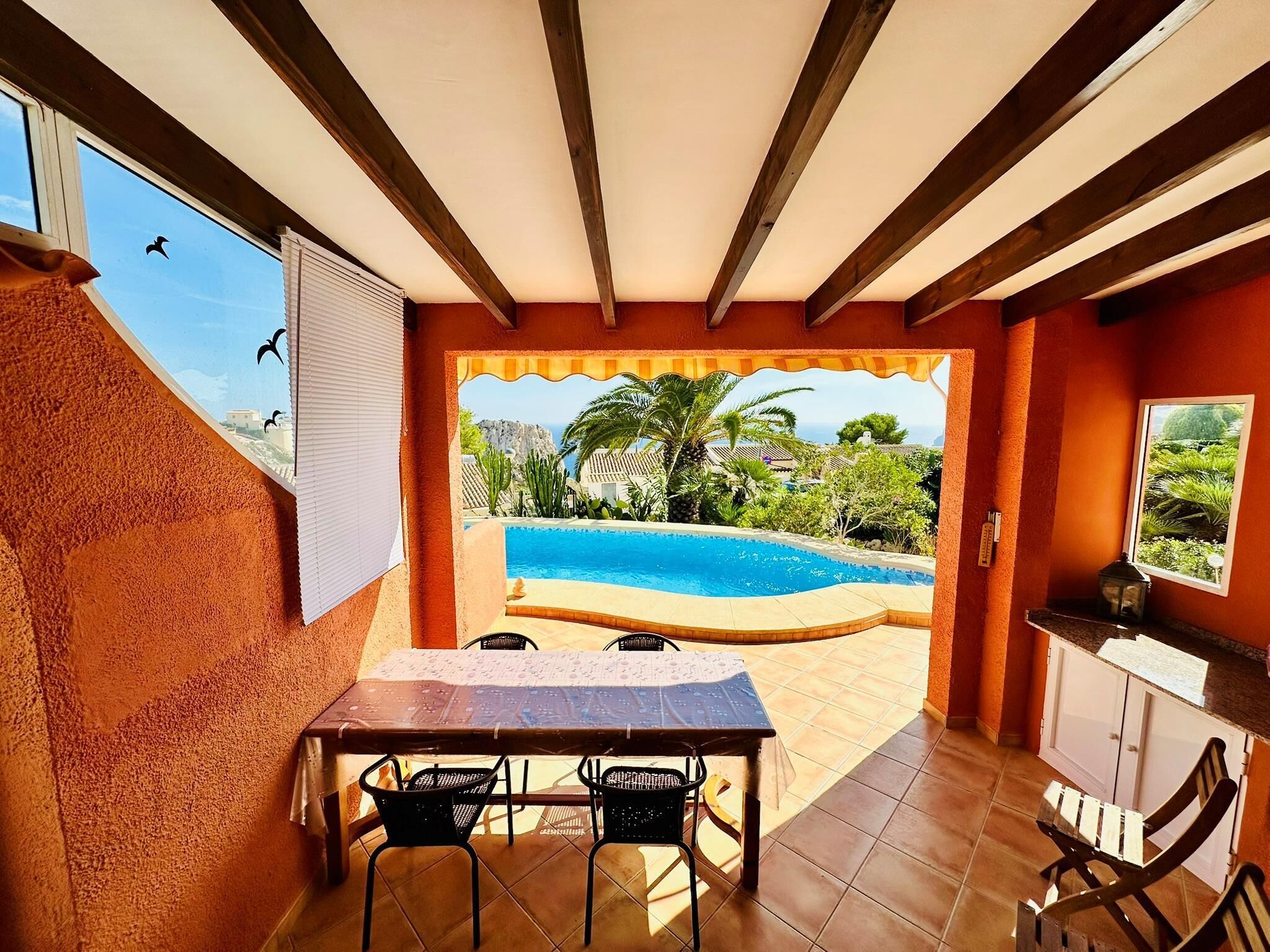 A room with a view of a swimming pool, a table with chairs, and a window with blinds.