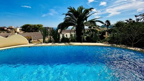A clear blue swimming pool surrounded by palm trees and buildings with tiled roofs.