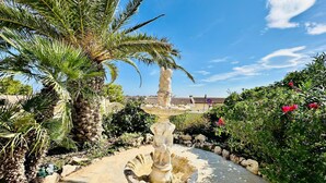 A garden with a stone fountain, palm trees, and a stone pathway.