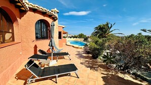 A patio with sun loungers, a pool, and a view of the surrounding landscape.