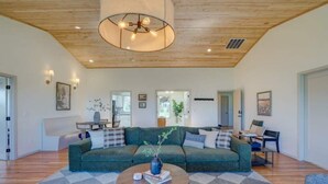 A spacious living room with a large green sofa, a round coffee table, and a wooden ceiling with recessed lighting. - Wilderness Ranch Retreat (Boise)