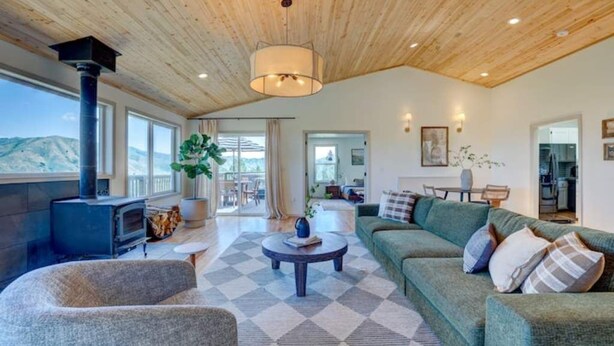 A spacious living room with a fireplace, a large sofa, a coffee table, and a view of the mountains. - Wilderness Ranch Retreat (Boise)