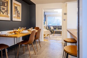 A modern dining area with a wooden table, chairs, and a sofa in the background. - Stylish 2 bedroom house in quiet suburb of Chester Sleeps 6 by Restfully (Blacon)