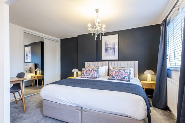 A modern hotel room with a large bed, bedside tables with lamps, a desk, and a chair. - Stylish 2 bedroom house in quiet suburb of Chester Sleeps 6 by Restfully (Blacon)