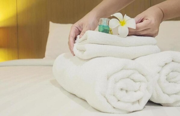 A neatly folded white towel on a bed with a white flower and a bottle of lotion. - Lamore Hotel Da Nang (Da Nang)
