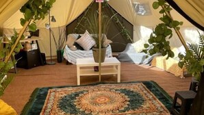 A cozy tent interior with a central seating area, a decorative rug, and potted plants. - Bell Tent Village (Nottingham)