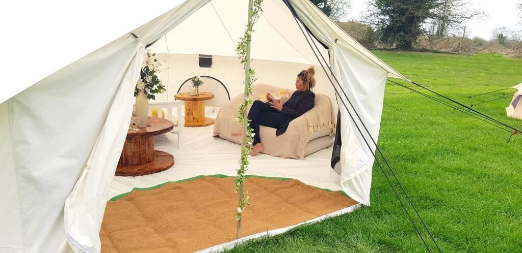 Uma tenda com uma pessoa sentada em um assento de bean bag, uma mesa de madeira redonda e uma pequena planta.