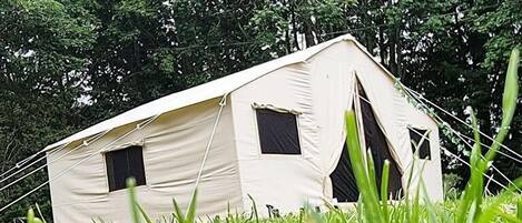 A tent with two windows, surrounded by tall grass and trees.