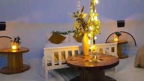 A cozy interior with a round wooden table, white cushioned seating, and decorative lighting. - Bell Tent Village (Nottingham)