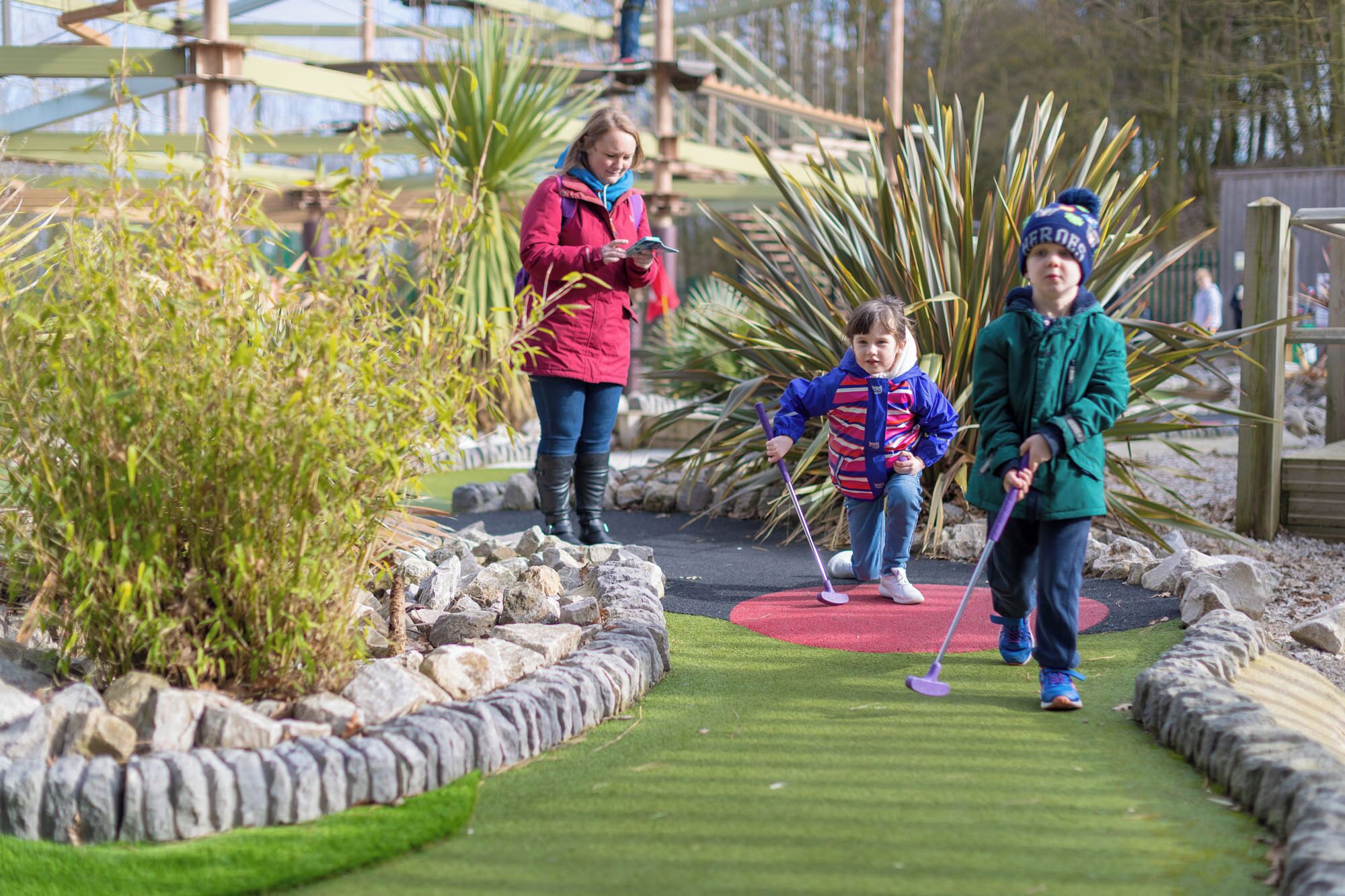 A miniature golf course with a green artificial turf, stone borders, and palm plants.